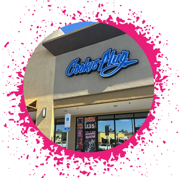 Cavalier-Estates-Cookie-Plug-bakery-in-Phoenix-AZ-order-cookies-for-delivery Tan storefront with a black, white, and blue sign that says 'Cookie Plug' with window decals that say 'Coming soon" and "Cookie Plug" with pictures of large, thick cookies in the window.